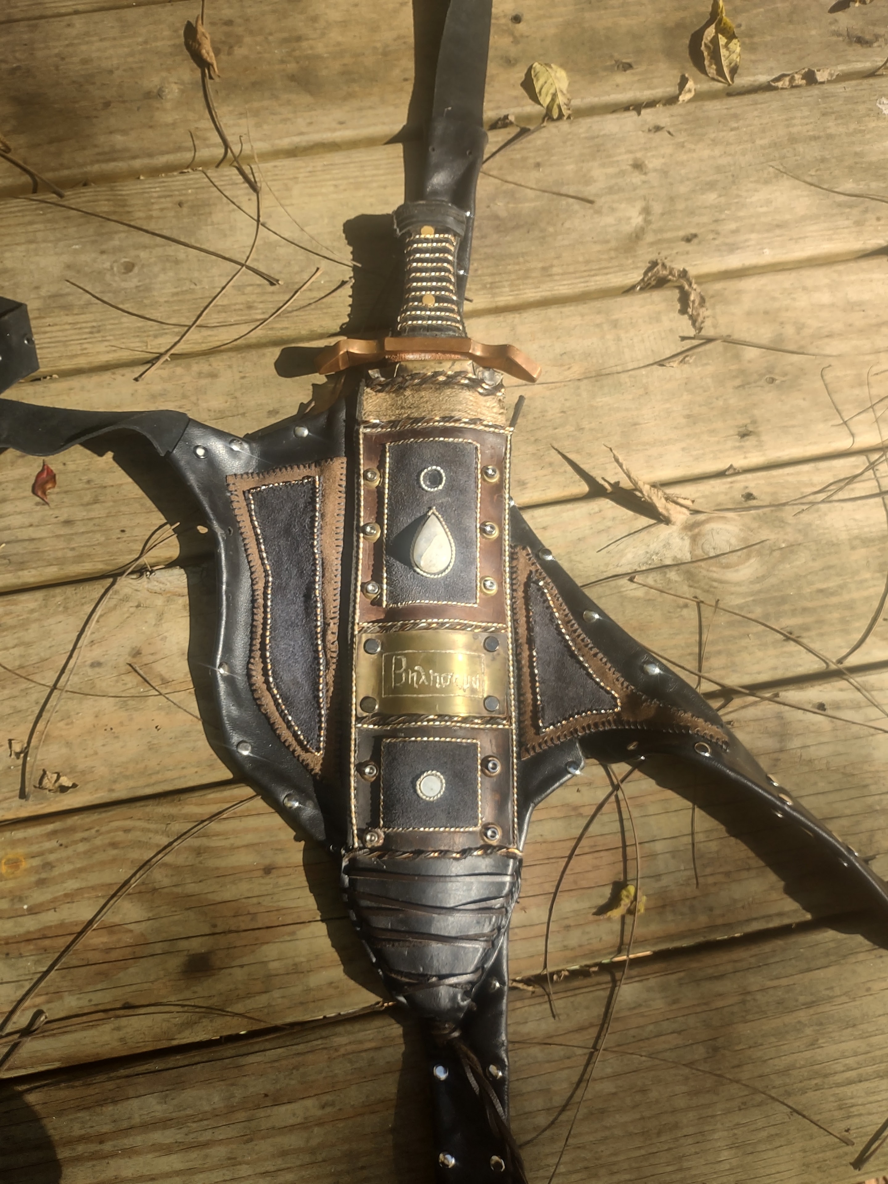 Decorative sword with ornate leather sheath and brass fittings on wood deck