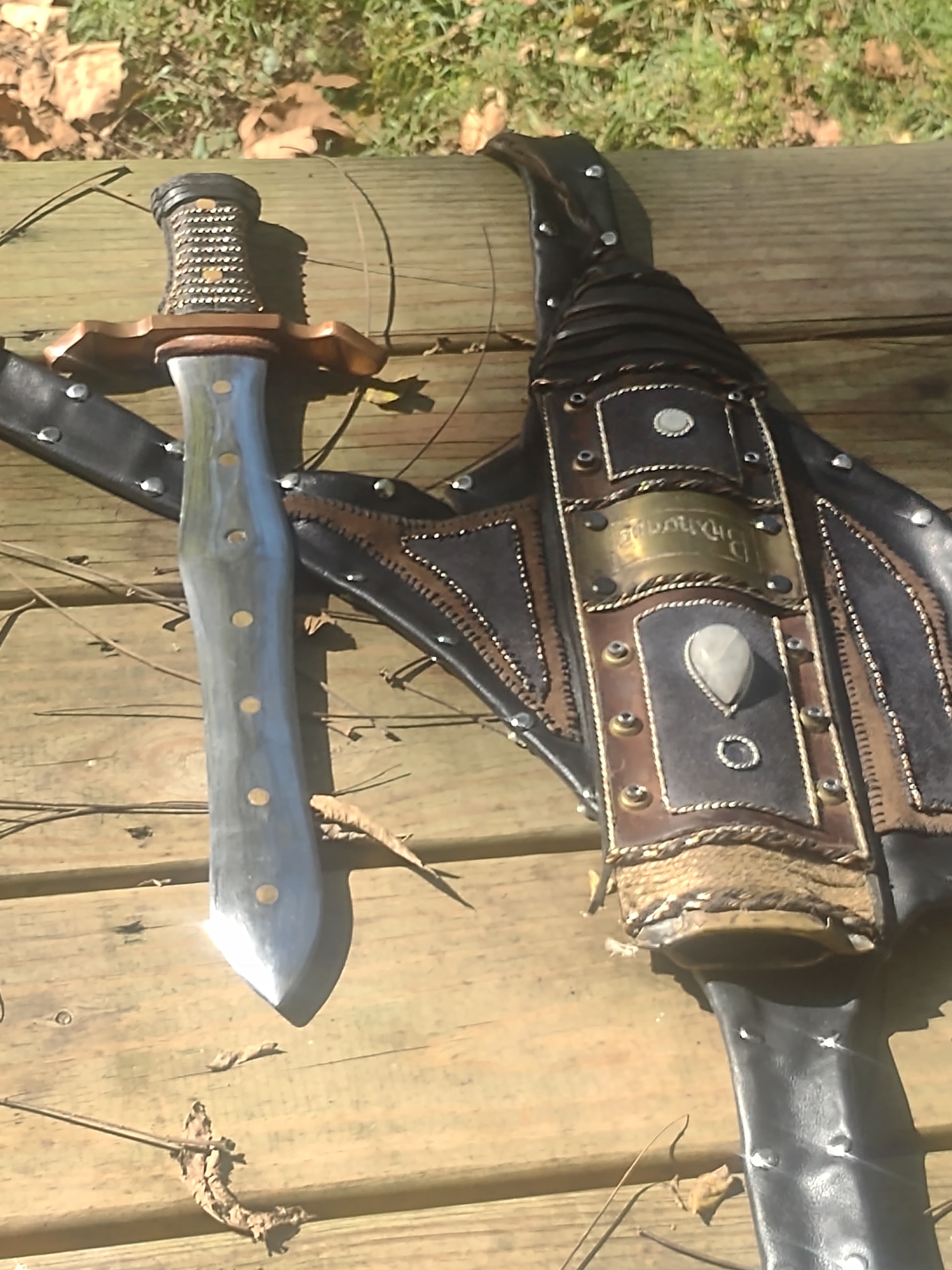 Blue-handled knife with copper guard beside ornate leather sheath on wood deck